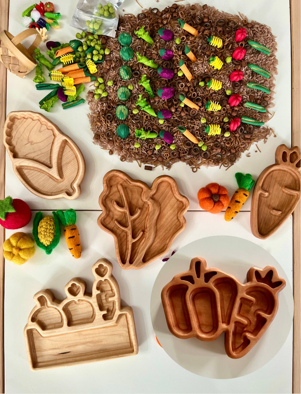 Wooden trays shaped like vegetables next to felt vegetable toys and brown spiral pasta on a white surface