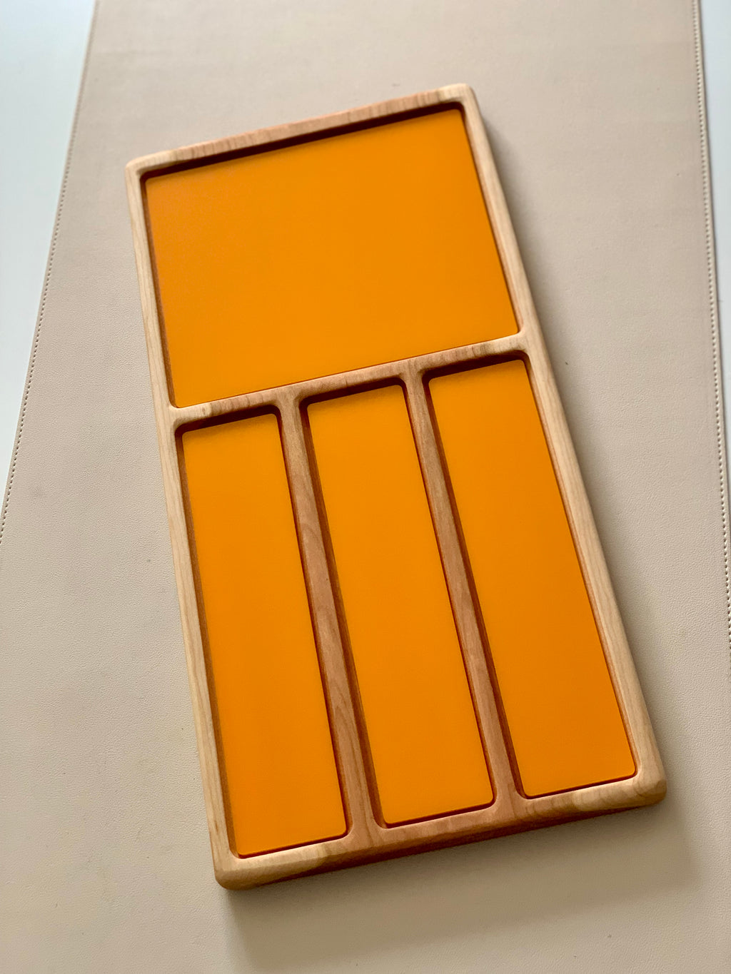 Wooden tray with one large square and three narrow rectangular orange panels on a light surface