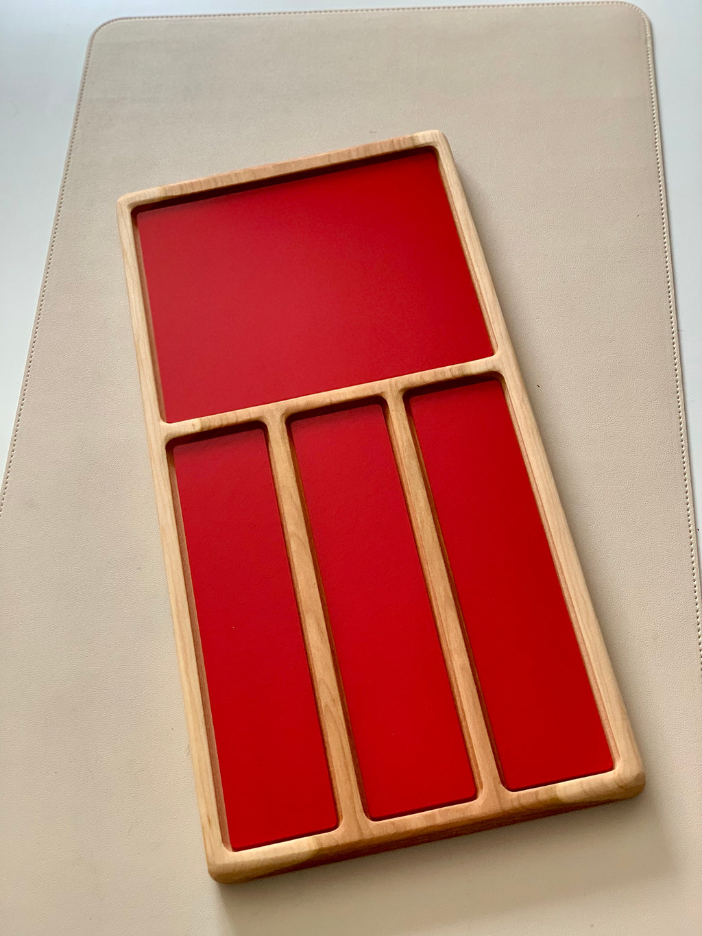 Wooden organizer tray with one large and three narrow deep compartments featuring red interiors on a beige surface