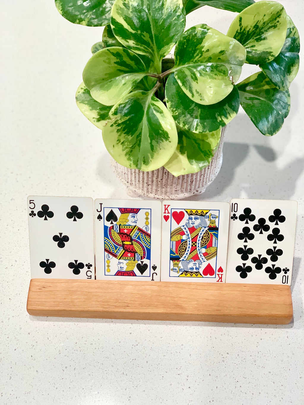 Extra long wooden flash card holder displaying four playing cards on white surface with potted green plant in background