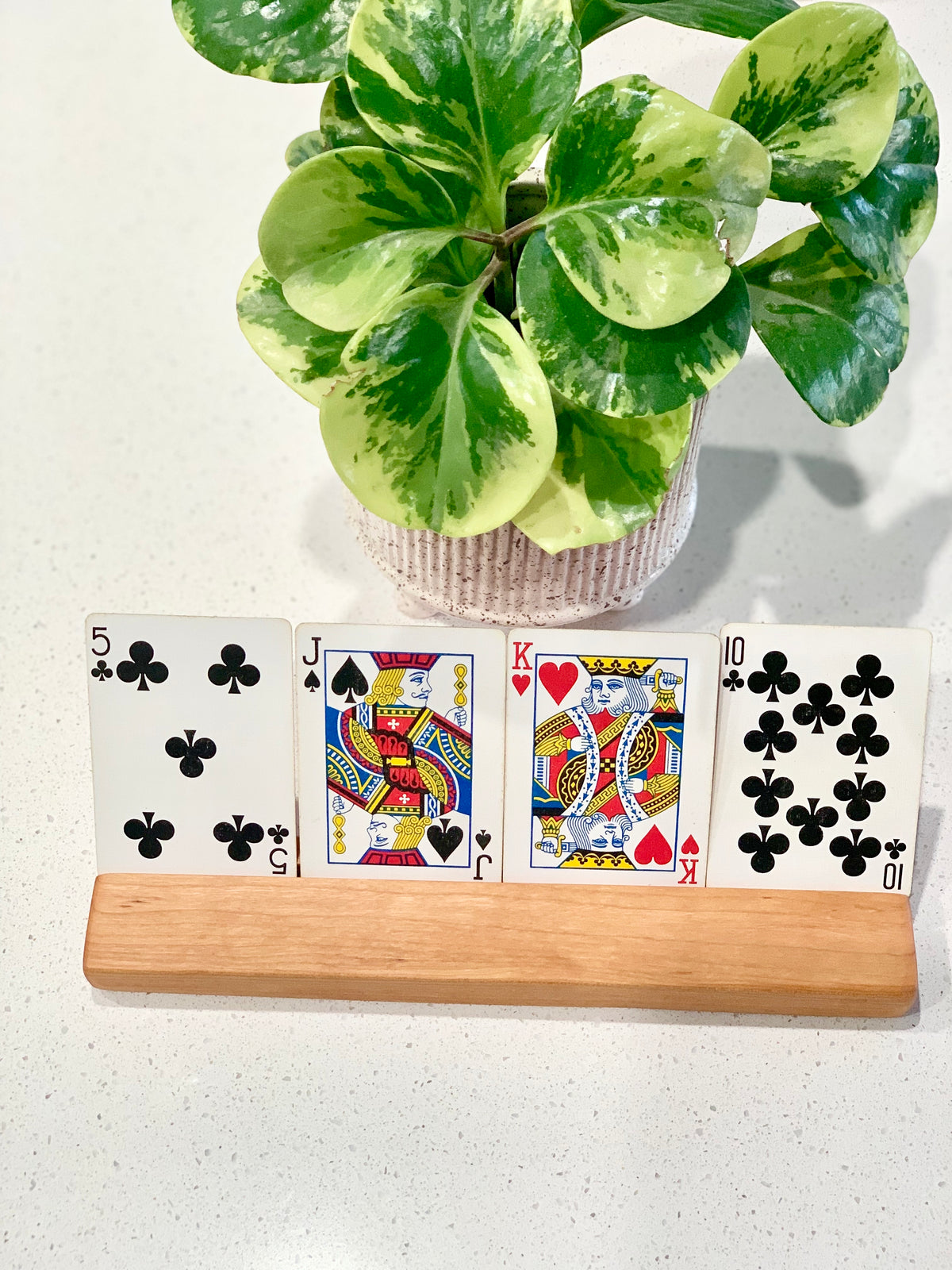 Extra long wooden flash card holder displaying four playing cards on white surface with potted green plant in background