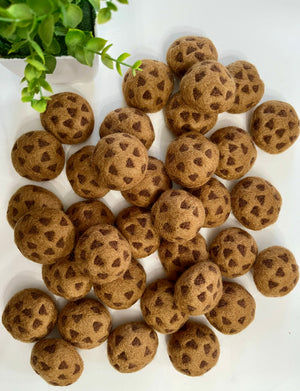 Scattered brown felt balls patterned with dark triangular shapes on white surface beside green plant leaves