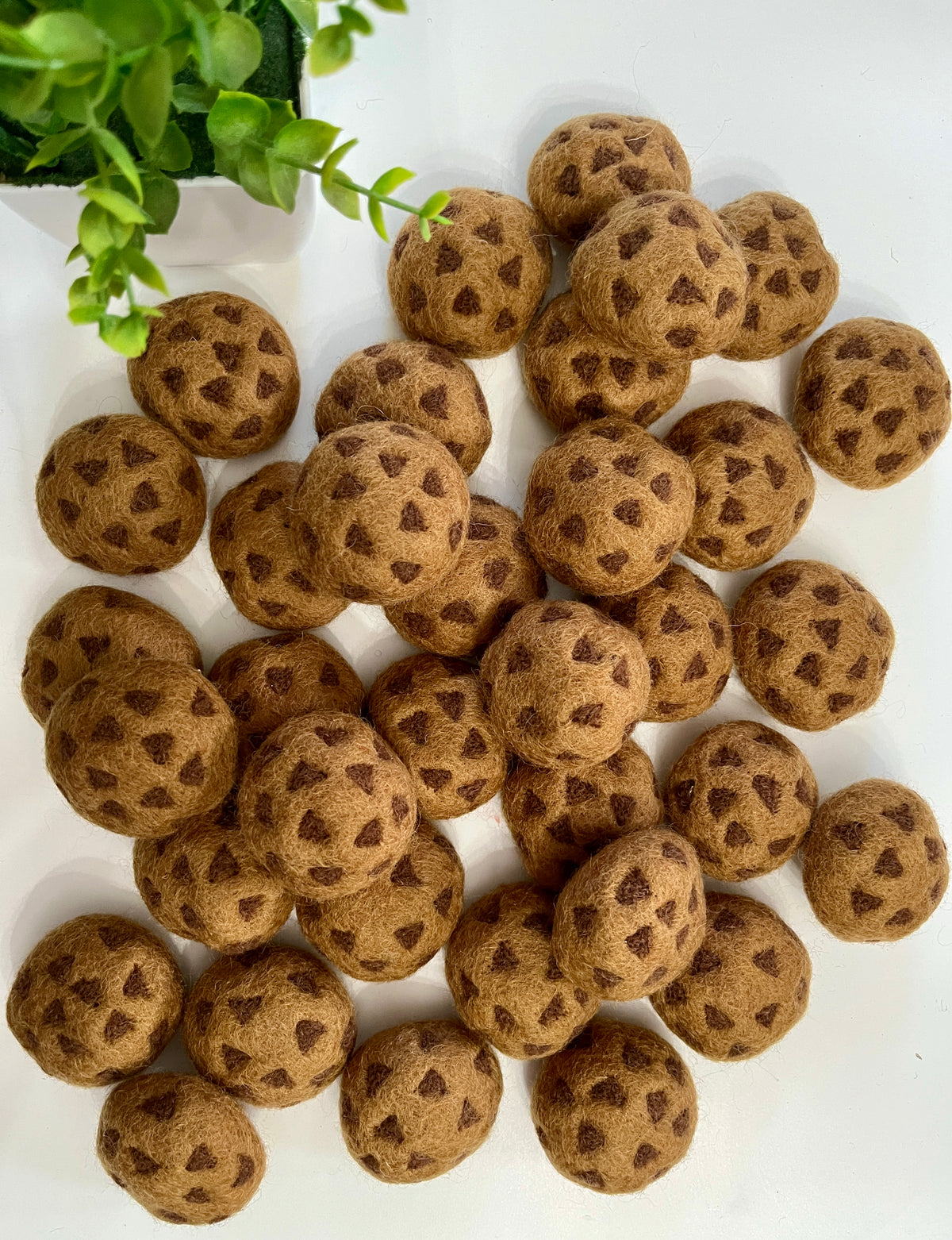 Scattered brown felt balls patterned with dark triangular shapes on white surface beside green plant leaves