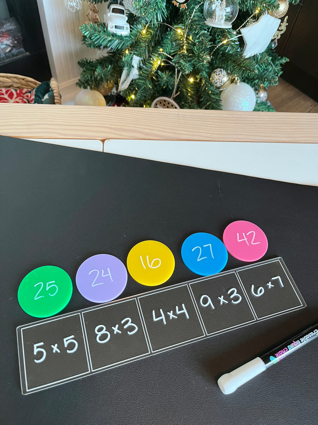 Blackboard surface with multiplication problems in white squares, colorful round counters showing corresponding answers, and a white marker nearby