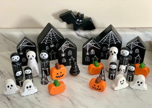 Wooden Halloween peg dolls including ghosts, skeletons, pumpkins, bats, and haunted houses on marble surface