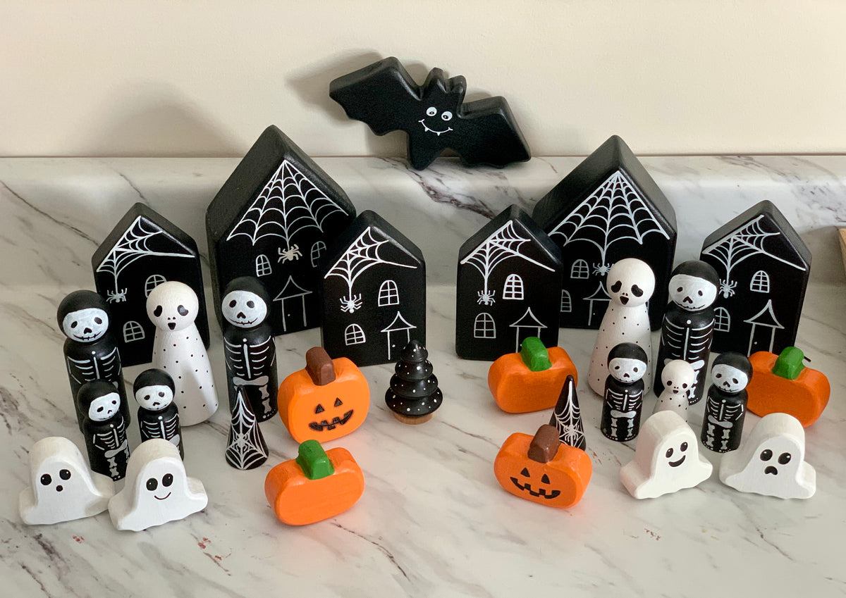 Wooden Halloween peg dolls including ghosts, skeletons, pumpkins, bats, and haunted houses on marble surface