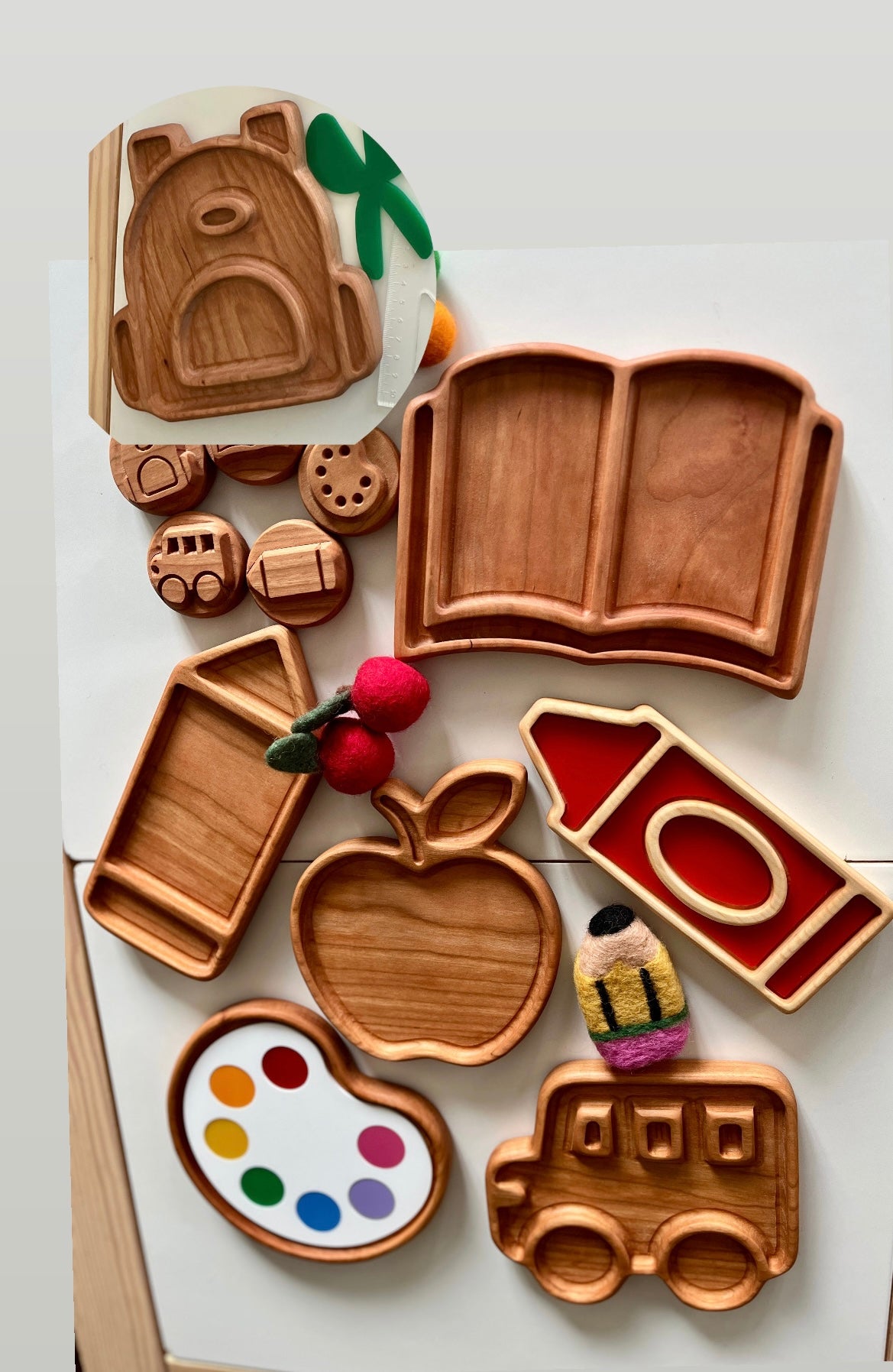 Carved wooden trays shaped like book, pencil, apple, crayon, artist palette, and school bus with small wooden and felt decorations