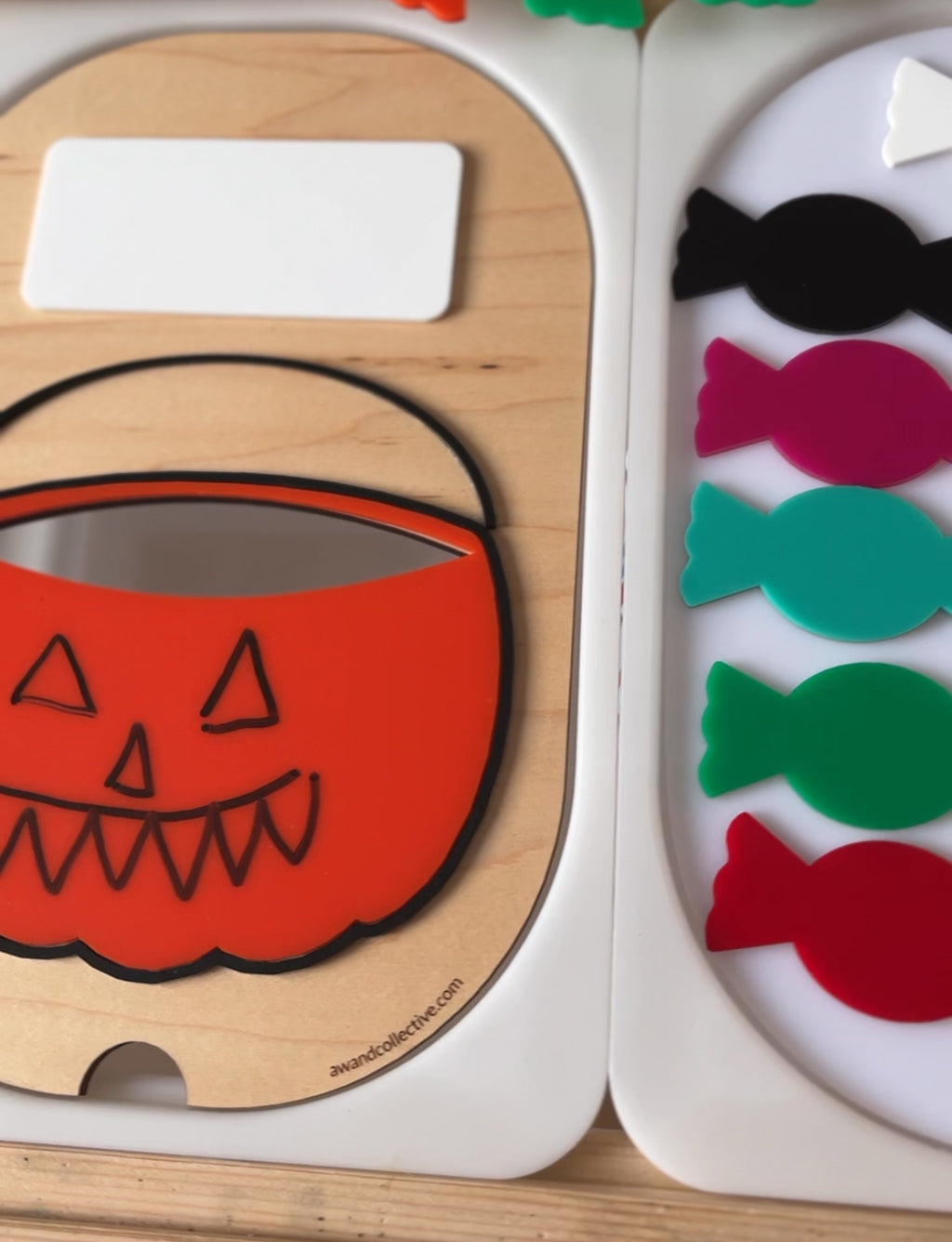 Close-up of a wooden Halloween-themed puzzle with an orange pumpkin basket and colorful candy-shaped pieces on a white tray