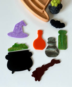 Assorted flat acrylic Halloween shapes including witch hat, cauldron, potion bottles, and broomstick on white surface