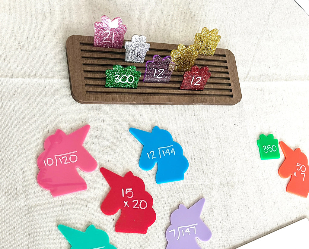 Colorful glittered gift-shaped pieces with numbers in a wooden tray above large plastic unicorn-shaped math learning tools, part of Little Dry Erasables - Set of 7 Large Unicorns, handcrafted homeschool education resources.