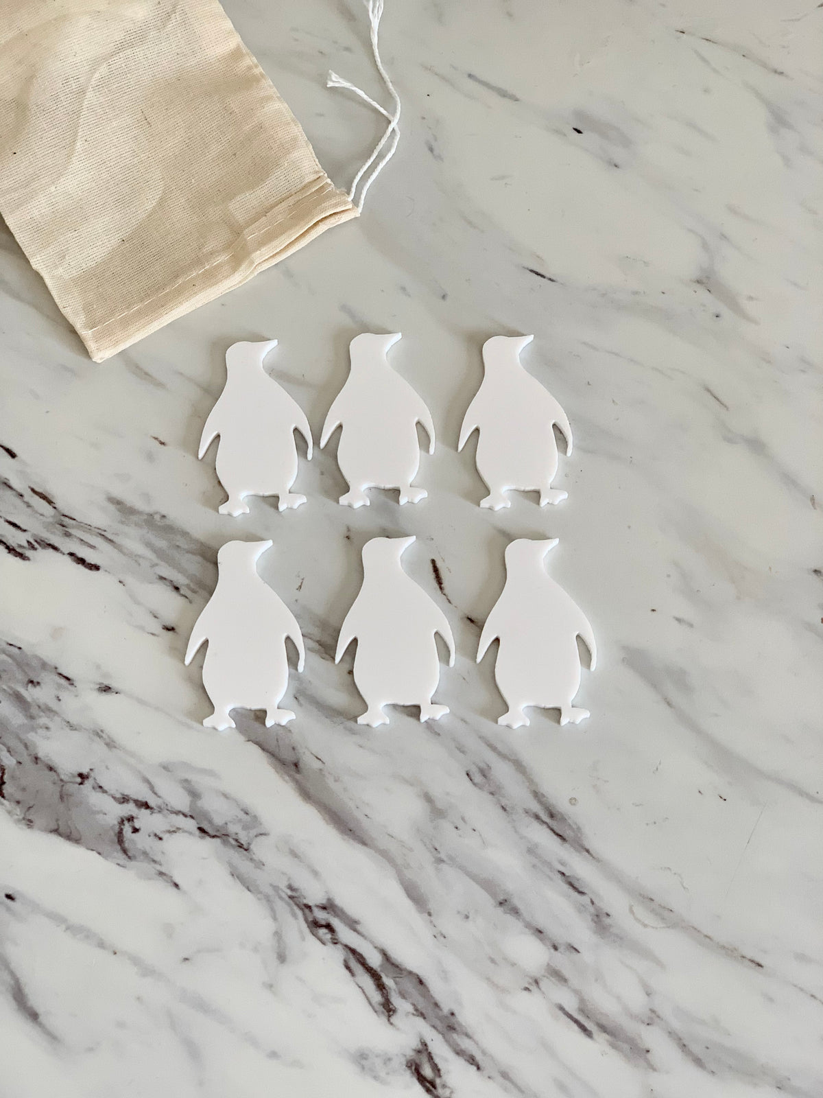 Set of six white penguin-shaped dry erasable boards with drawstring cotton pouch on marble surface
