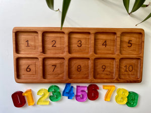 Wooden tray with ten numbered square slots from 1 to 10 and colorful translucent number pieces below on white surface