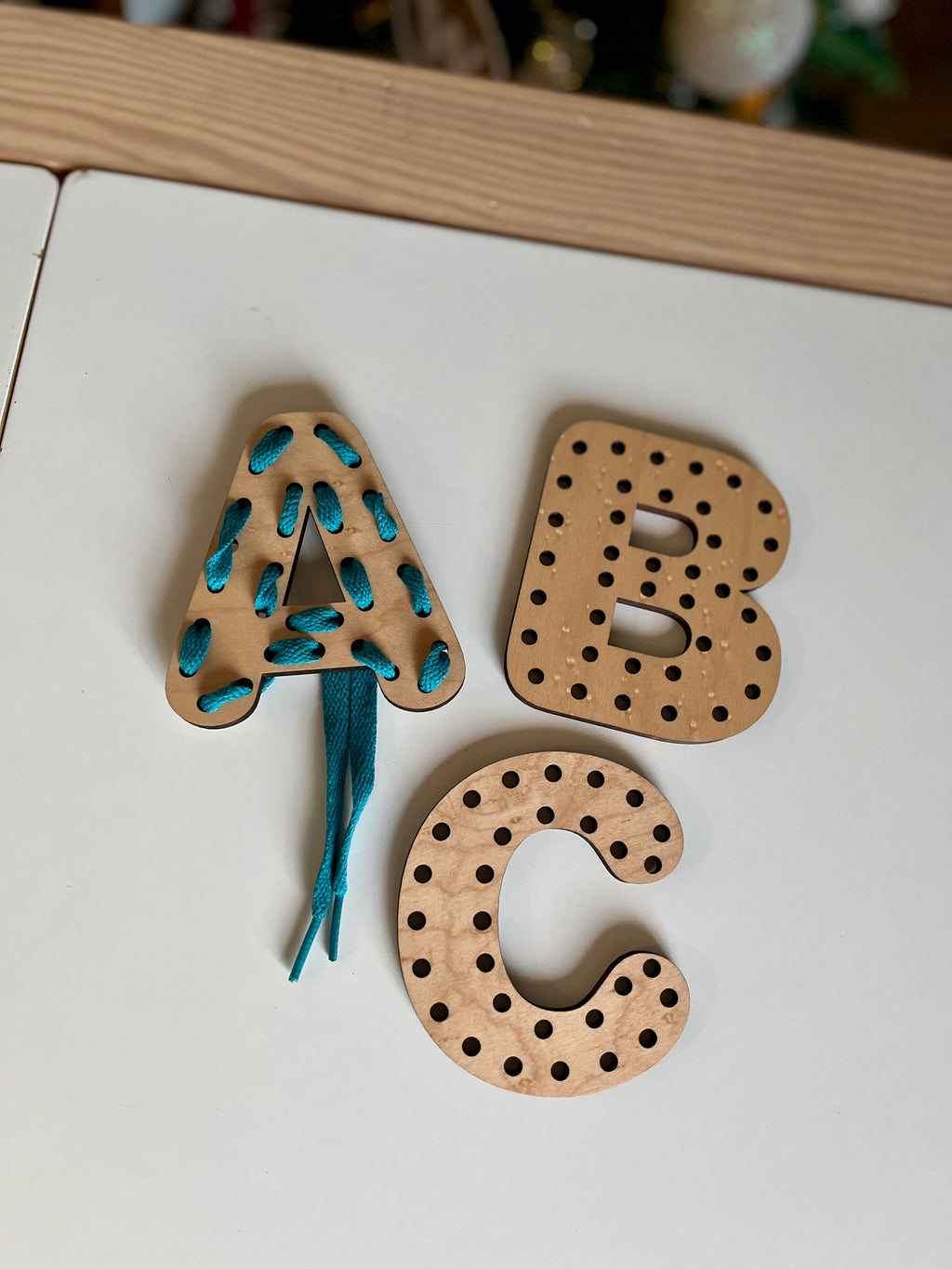 Three wooden Alphabet Lacing Letters (A, B, C shown — full alphabet optional) with holes for threading, featuring a blue lace in the letter A, handcrafted homeschool education resources.