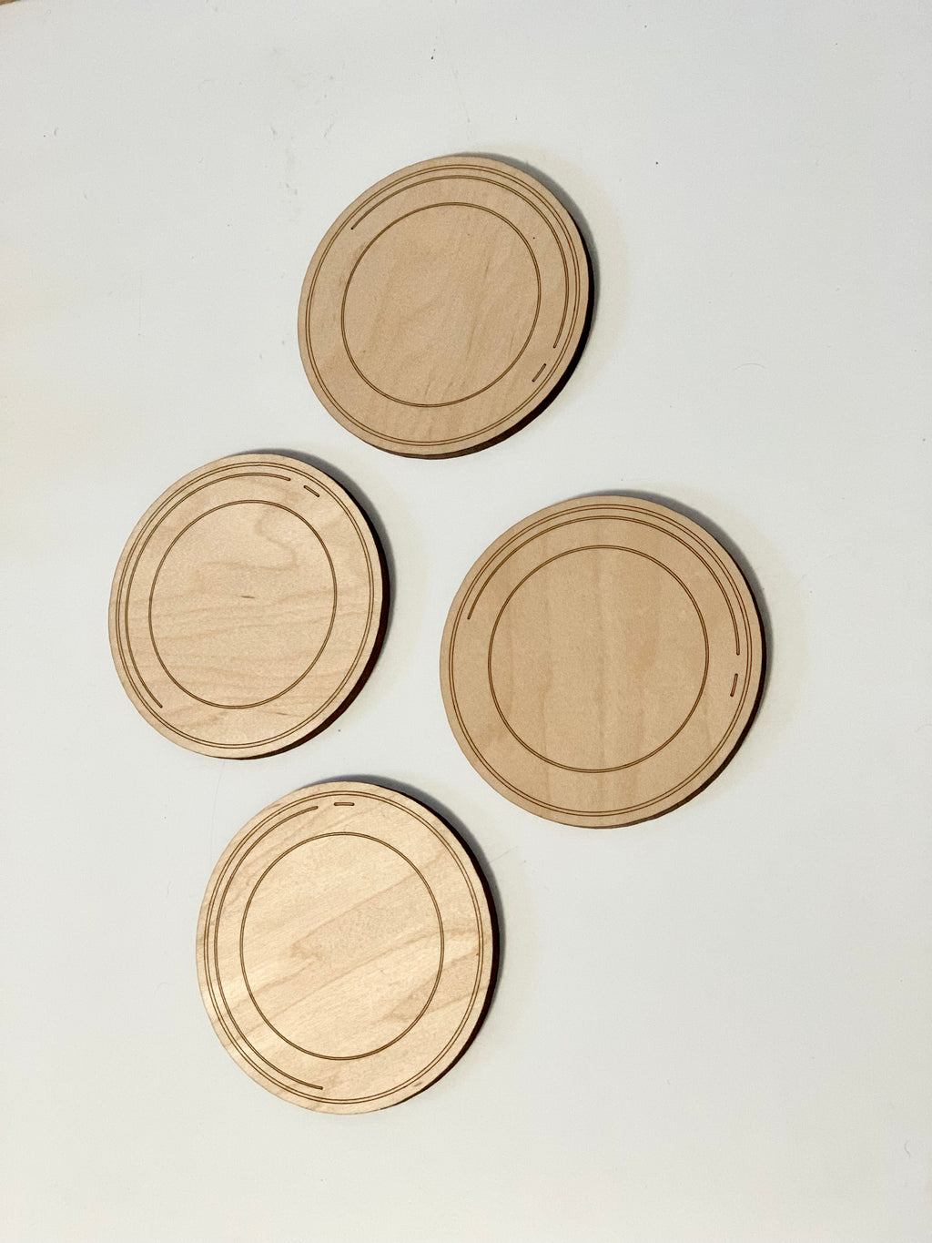 Set of four round flat wooden dishes with engraved circular patterns on light background