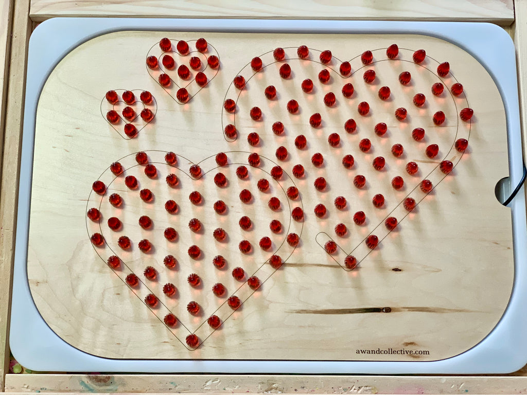 Wooden board with four heart outlines filled with removable red pegs on a light wood background.