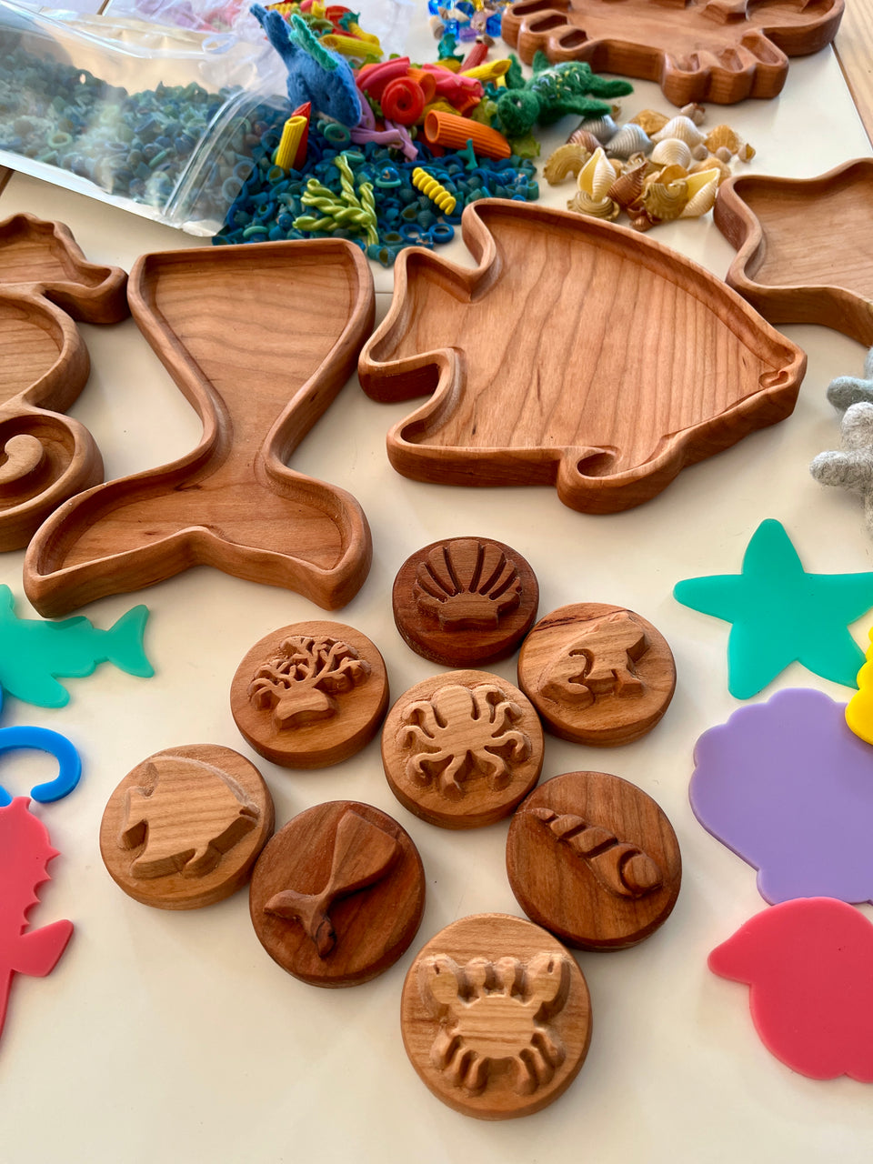 Wooden trays shaped like a seahorse and fish with round wooden sea creature stamps and colorful craft pieces on table