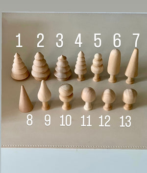 Thirteen small unfinished natural wood shapes including trees, cones, and rounded figures arranged on a neutral surface