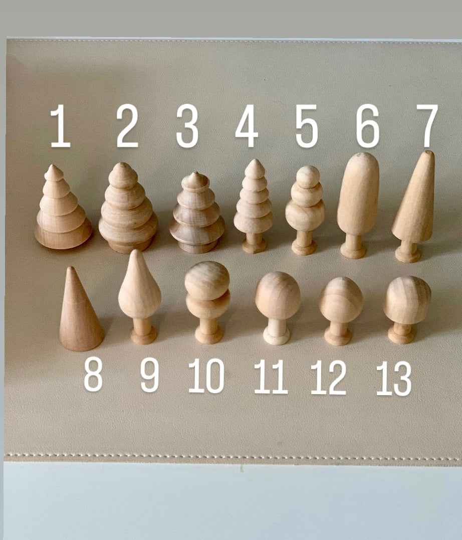 Thirteen small unfinished natural wood shapes including trees, cones, and rounded figures arranged on a neutral surface