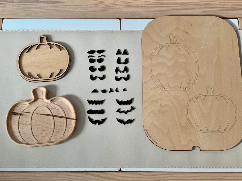 Laser cut pumpkin-shaped wooden sensory trays with carved pumpkin faces and removable facial feature pieces on table mat