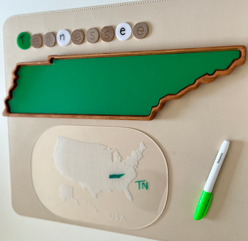 Green wooden tray shaped like Tennessee with letter tokens spelling Tennessee and a dry erase marker on beige surface
