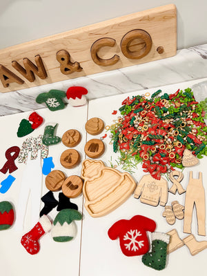 Assorted wooden and felt winter-themed shapes arranged near colorful pasta on a white marble surface