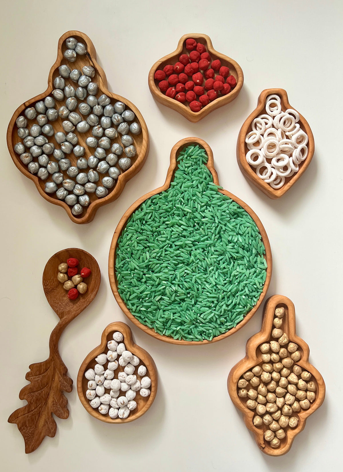 Set of wooden ornament-shaped trays filled with colorful beads, rice, and small decorative items on white background
