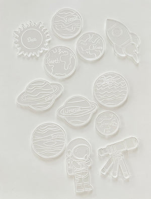 Clear plastic cookie cutters shaped like the sun, planets, an astronaut, rocket, and telescope on white background