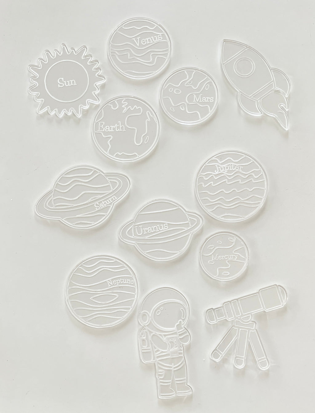 Clear plastic cookie cutters shaped like the sun, planets, an astronaut, rocket, and telescope on white background