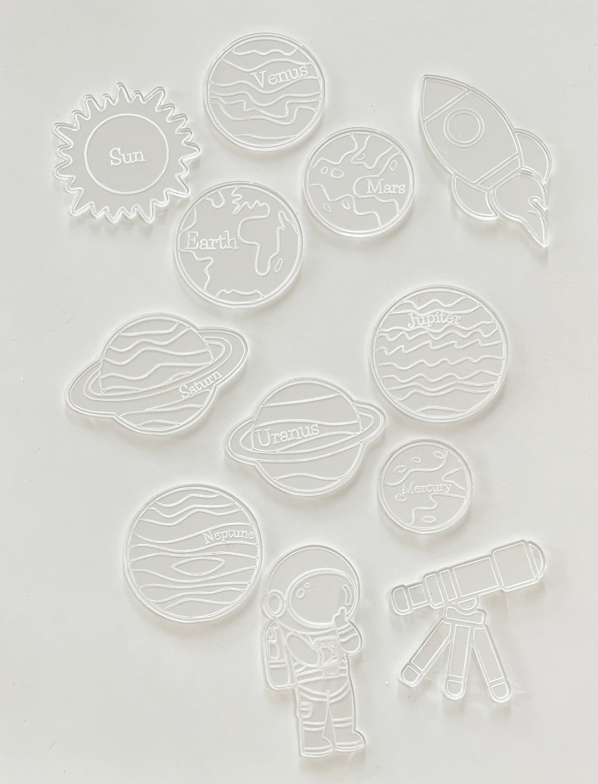 Clear plastic cookie cutters shaped like the sun, planets, an astronaut, rocket, and telescope on white background