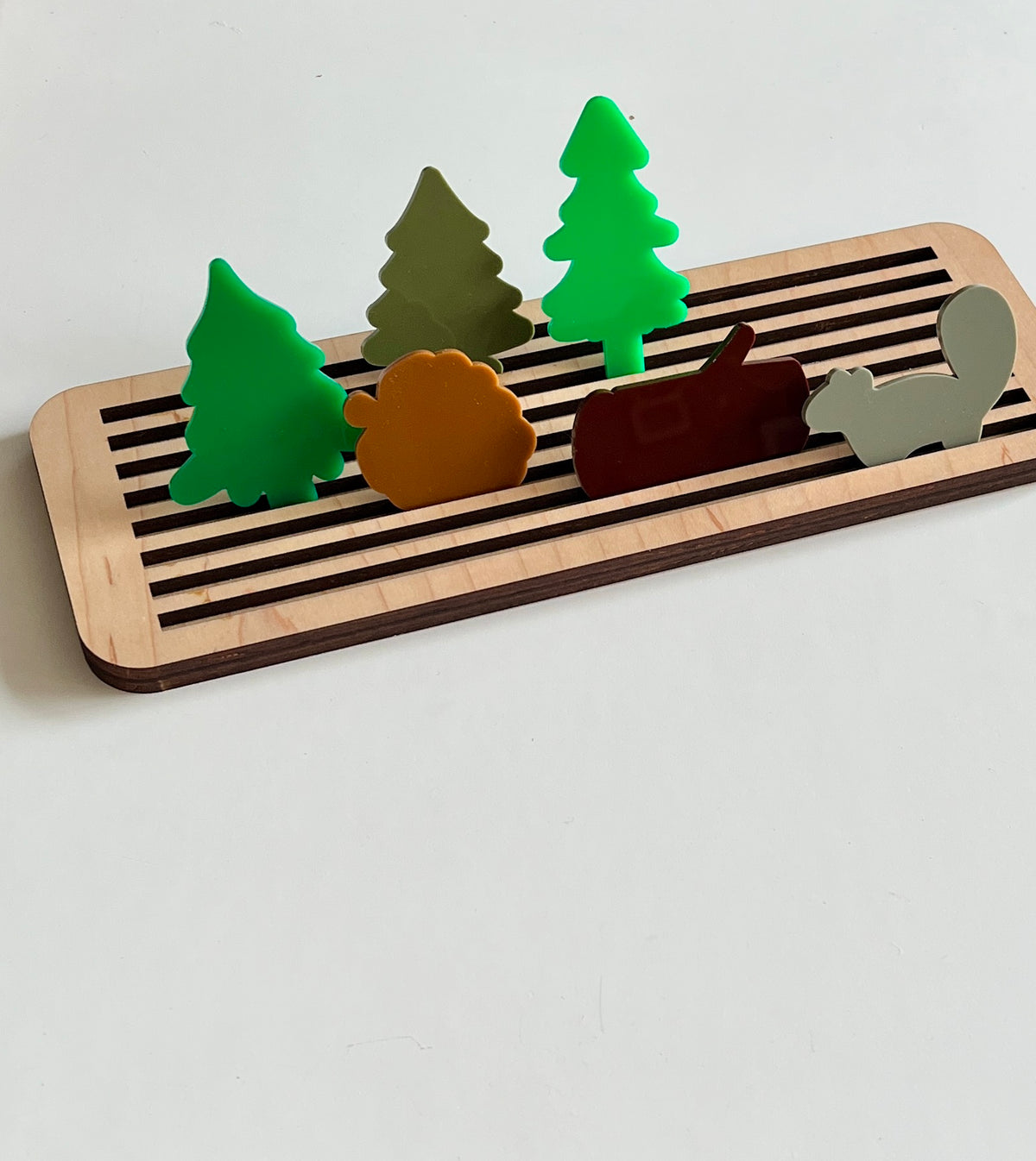 Wooden tray with grooves holding colorful acrylic forest-themed figures including trees, a hedgehog, a beaver, and a squirrel