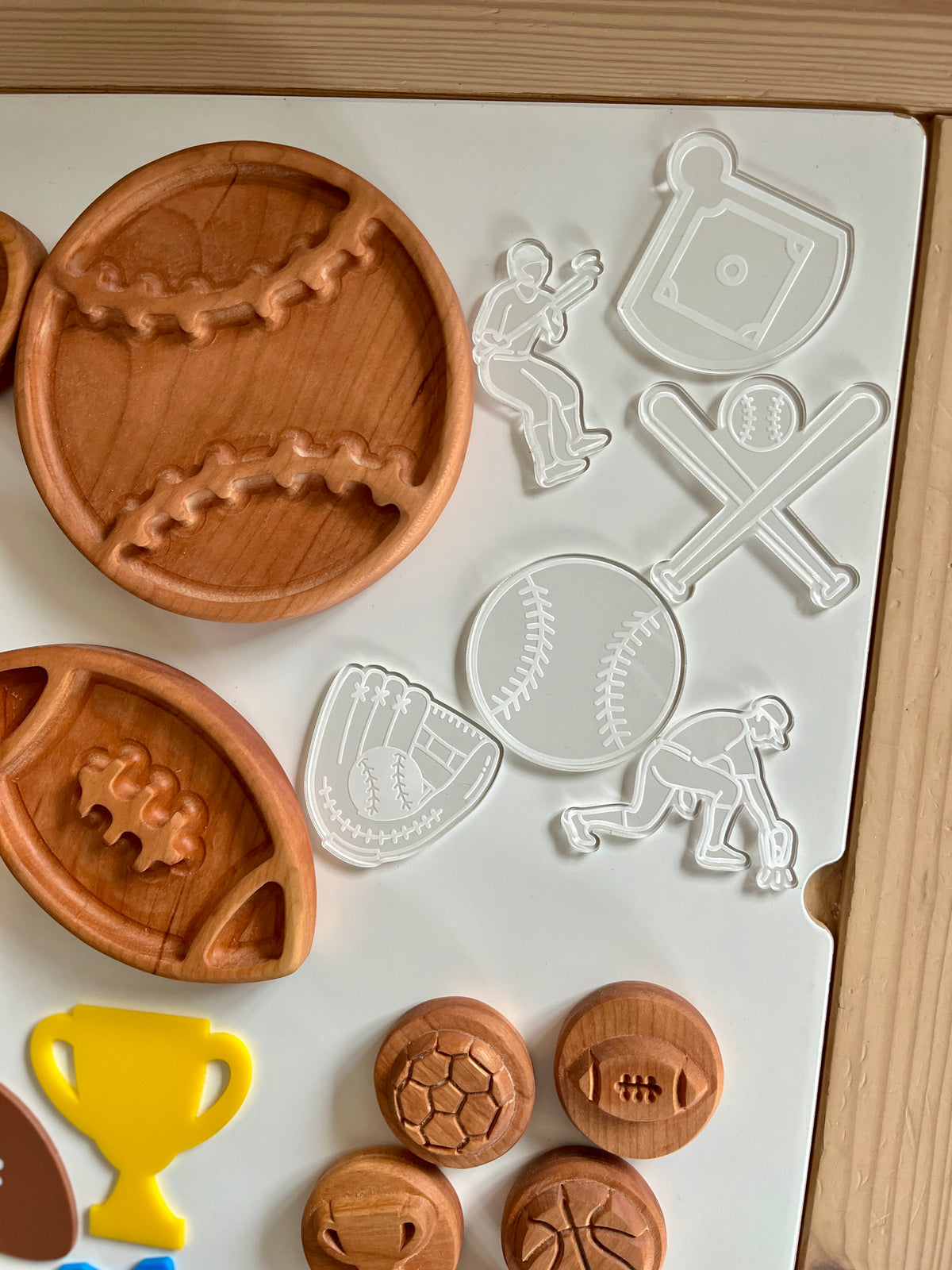 Clear plastic sports-themed cookie cutters with wooden trays shaped like a baseball and football on a white board