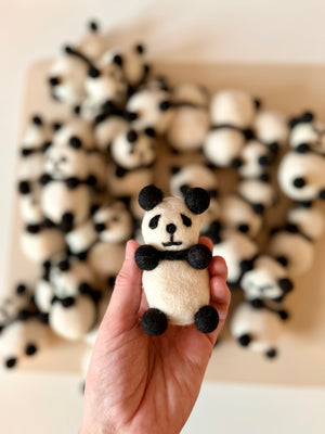 Hand holding a small handcrafted felt panda with black and white details over a blurred group of similar pandas