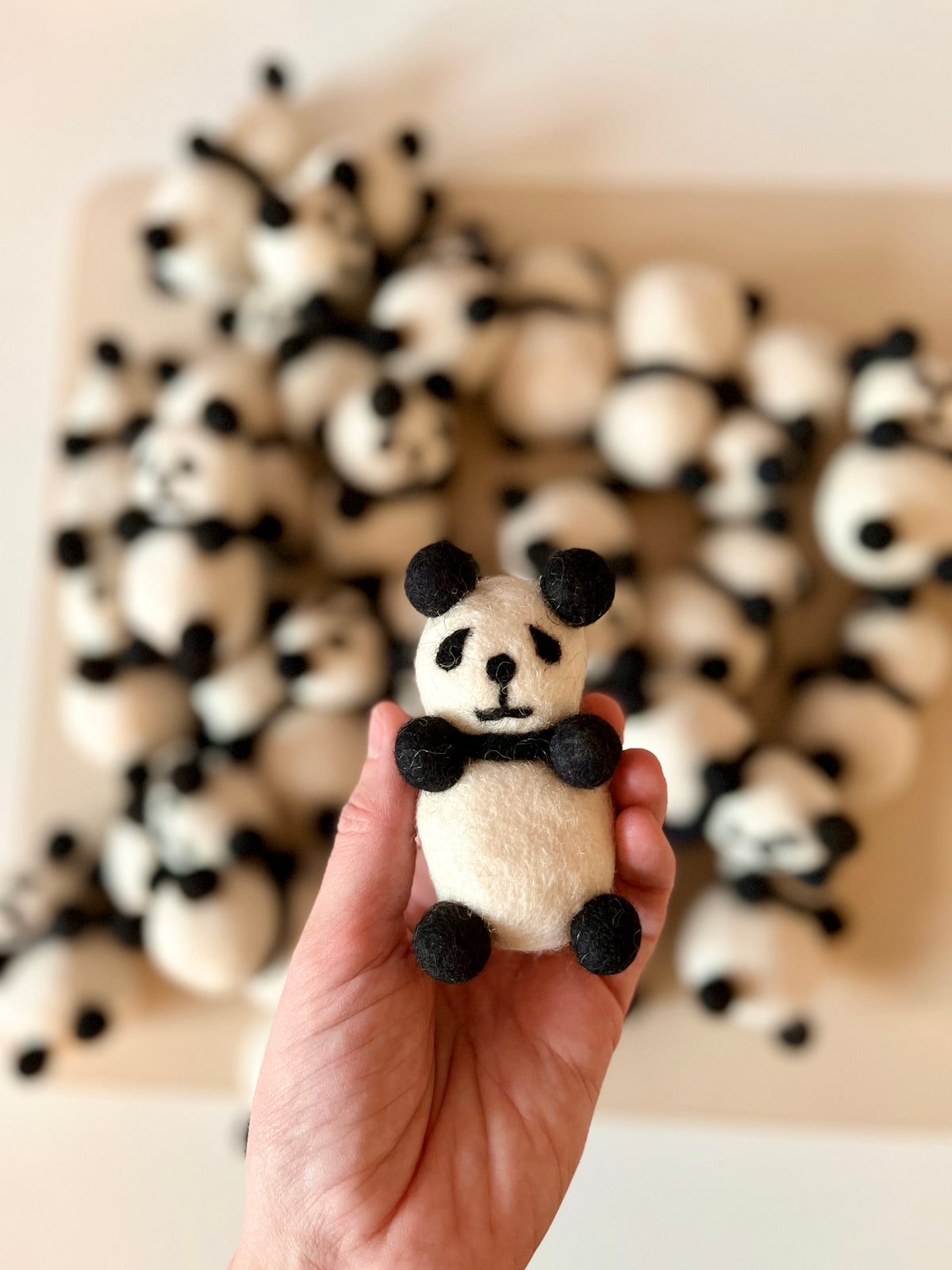 Hand holding a small handcrafted felt panda with black and white details over a blurred group of similar pandas