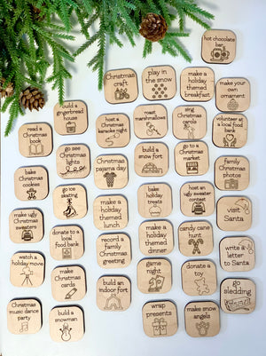 Wooden Christmas activity tokens with holiday-themed illustrations arranged on white surface with pine branches and pinecones nearby