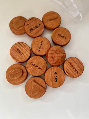 Round wooden tokens engraved with various geometric shapes and their names on a white surface