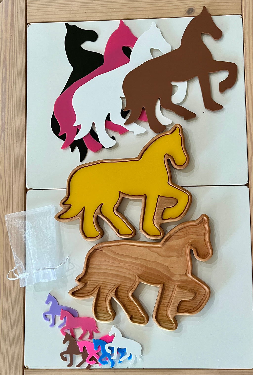 Stack of horse-shaped trays and small cutouts in multiple colors including yellow, brown, black, white, pink, and purple on wooden table