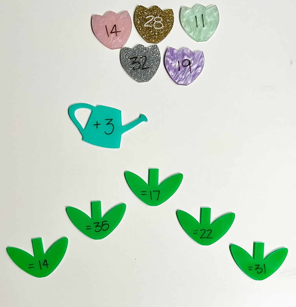 Little Dry Erasables - 2 Part Marble / Glitter Flowers with Watering Can featuring colorful marble and glitter flower pieces with handwritten numbers, teal watering can with math equation, and green leaf-shaped pieces with sums, handcrafted homeschool education resources.