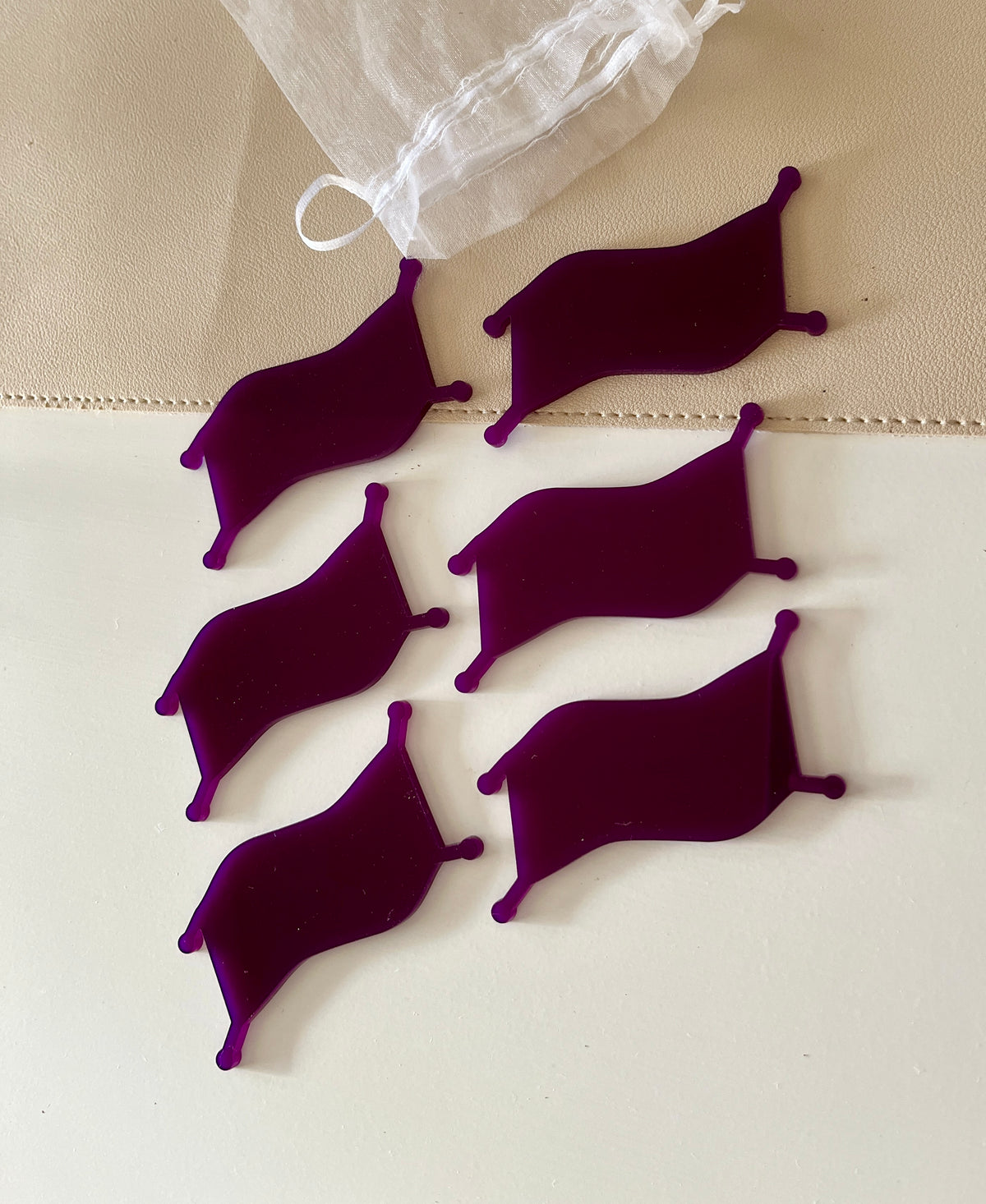 Six deep purple velvet patches with rounded tips arranged near a sheer white drawstring pouch on a beige surface