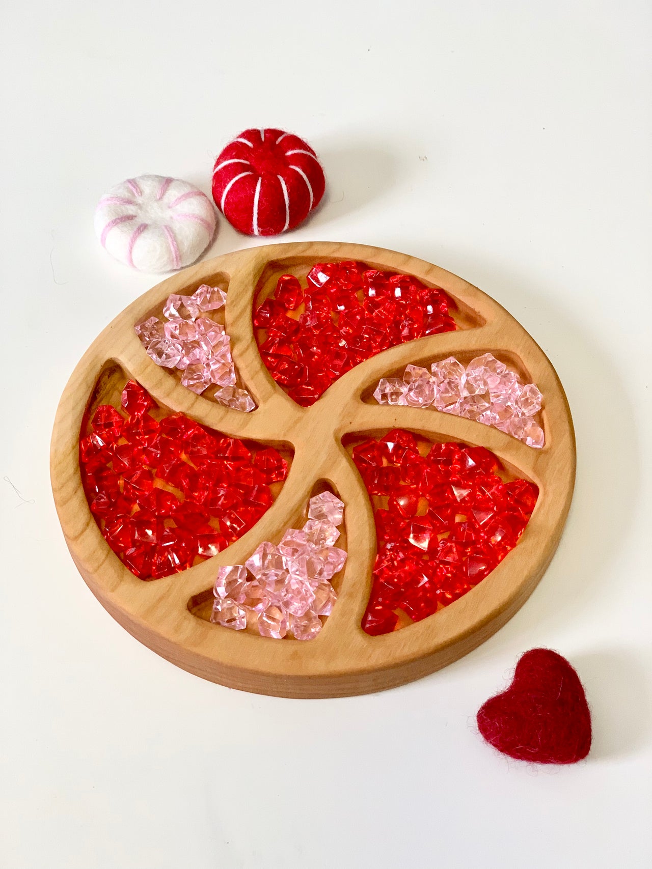 Round wooden tray with red and pink acrylic gems and three felt decorations on white surface