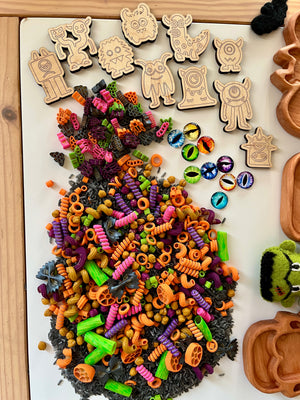 Wooden monster tokens with colorful spiral pasta, plastic monster eye pieces, and wooden trays on light surface