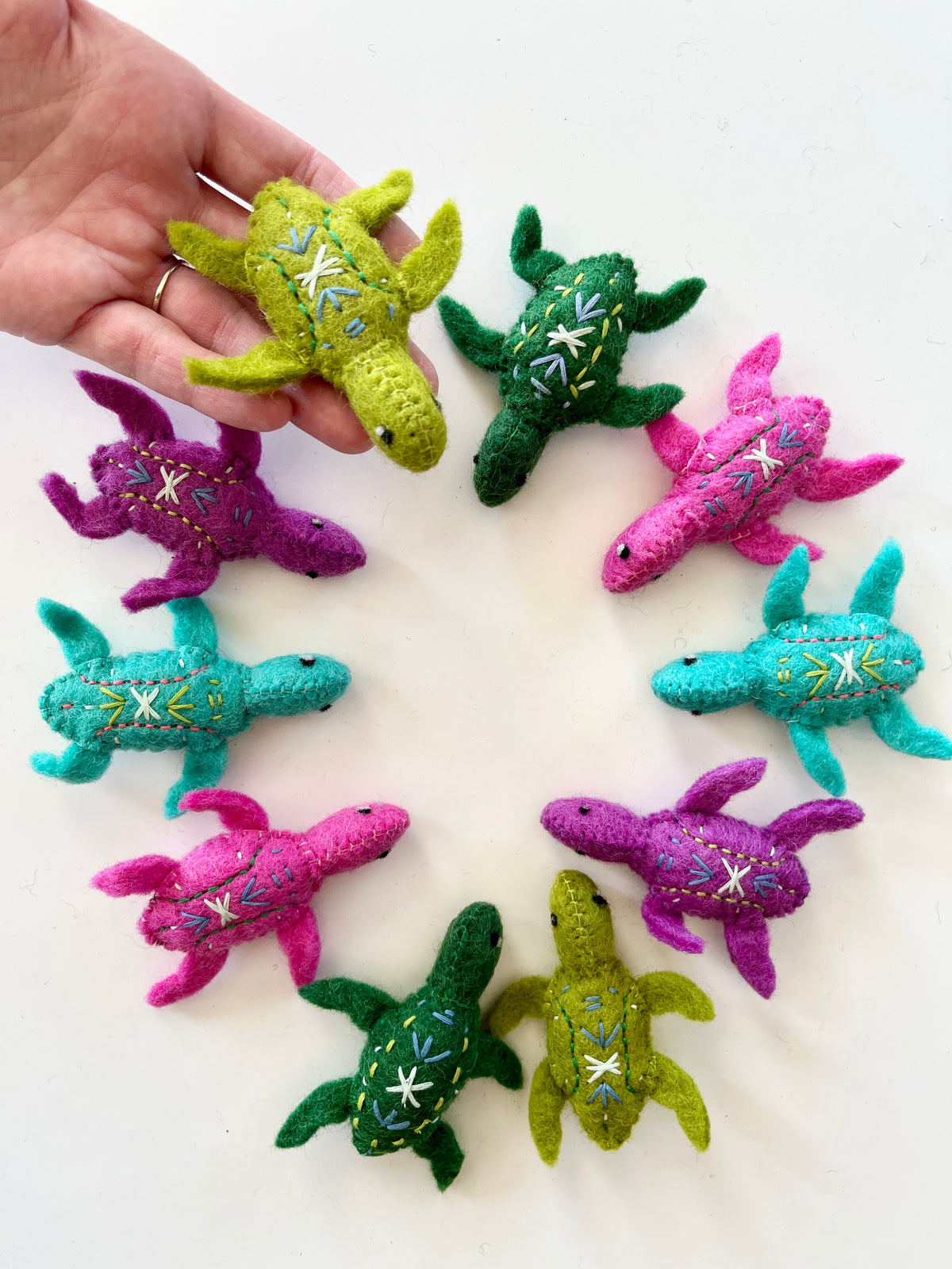Assorted colorful handmade felt turtles with embroidered shell details arranged in a circle on a white background