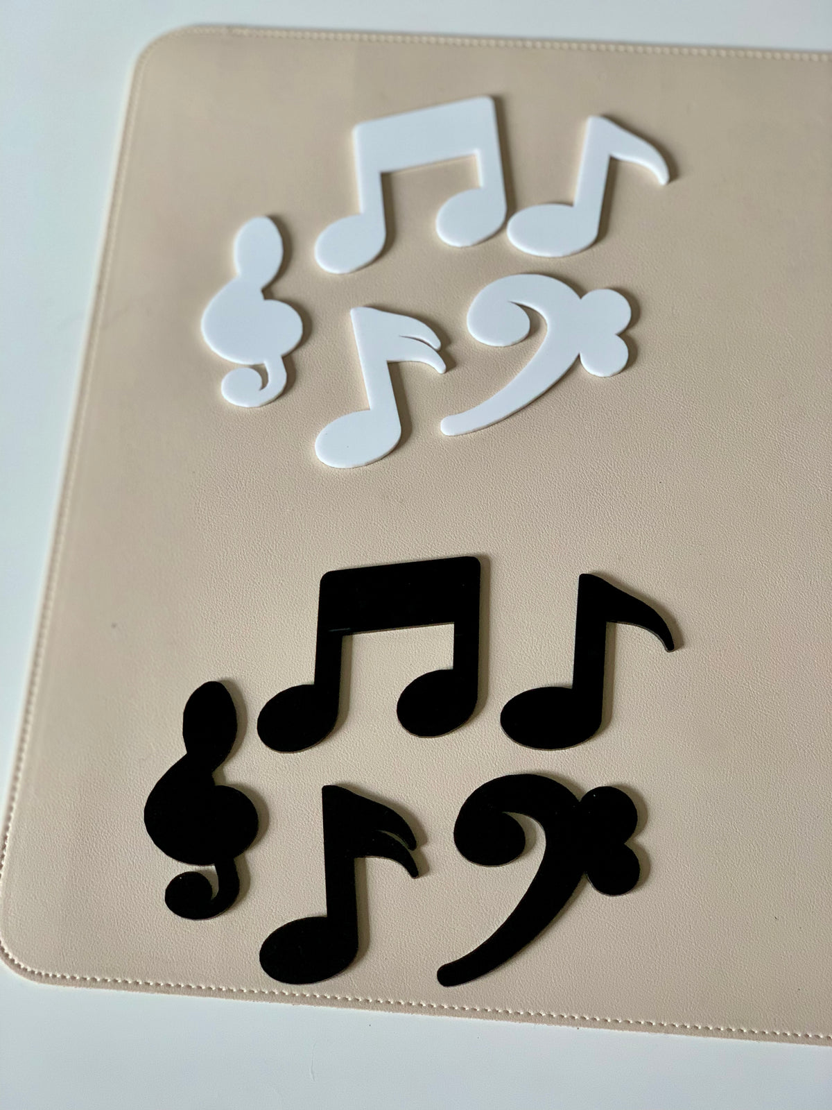 Black and white plastic music note and clef shapes arranged on a beige surface in two groups