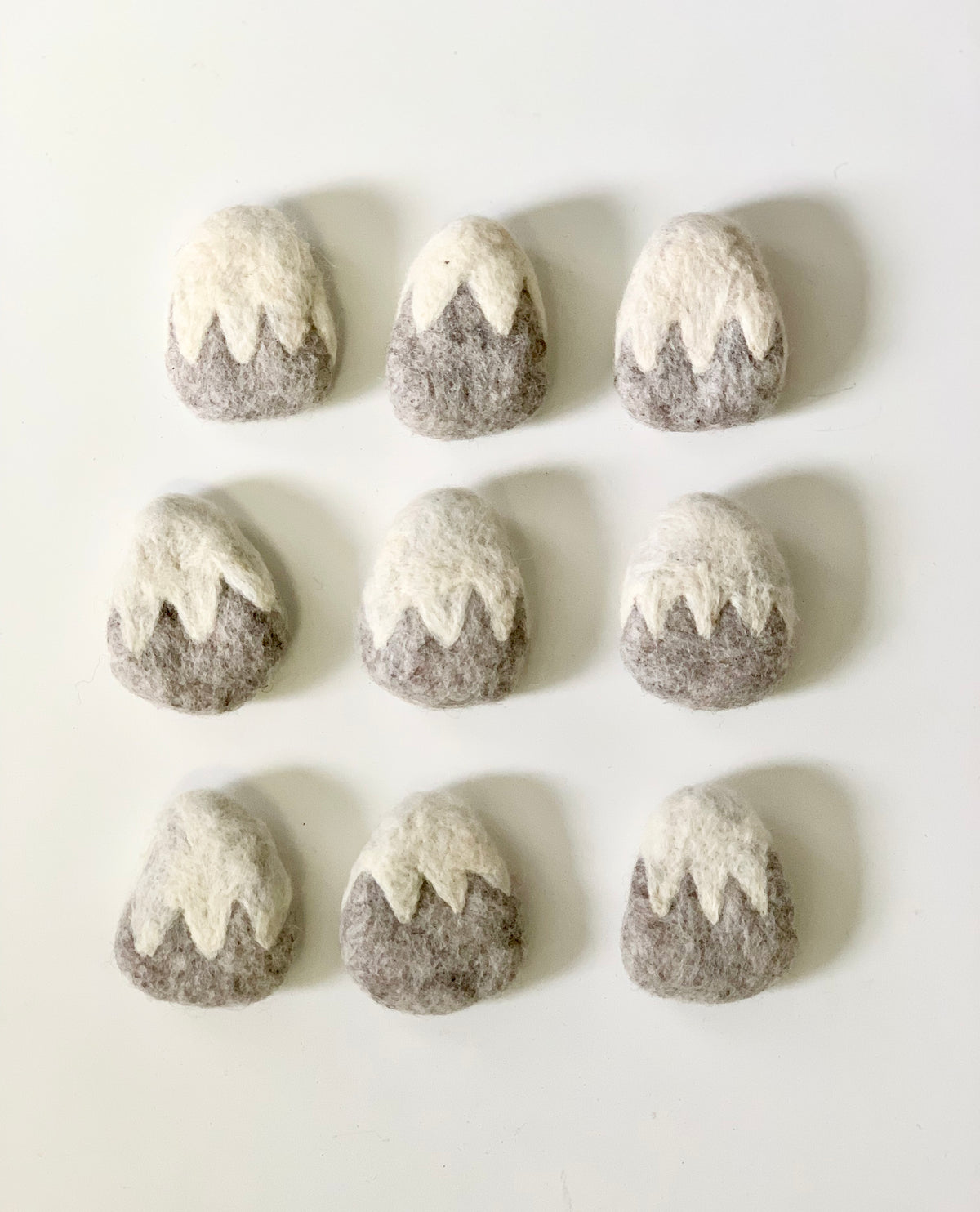 Nine handmade grey felt mountains with white snowy peaks arranged in three rows on white background