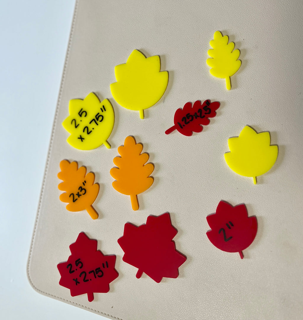 Assorted yellow, orange, and red leaf-shaped cutouts with handwritten size markings on a beige surface