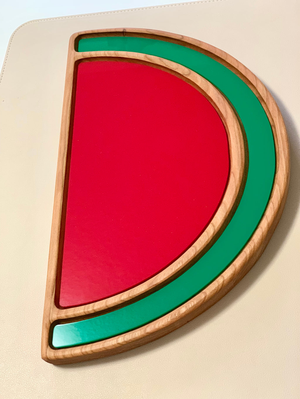 Wooden watermelon-shaped sensory tray with red and green painted sections on light background