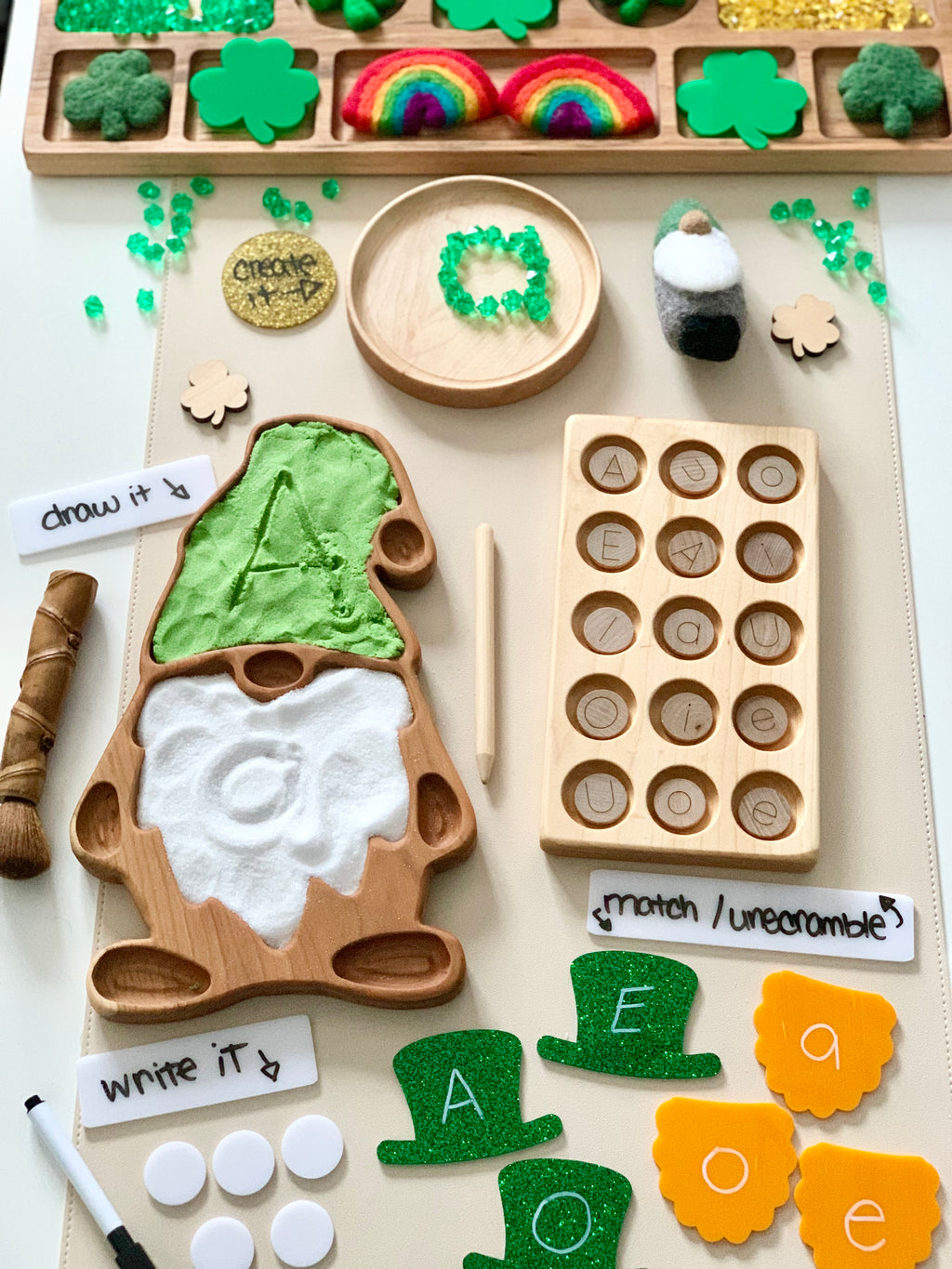 Wooden gnome tray with sand showing the letter A, wooden board with letter tokens, felt rainbows, and letter practice cards on a table