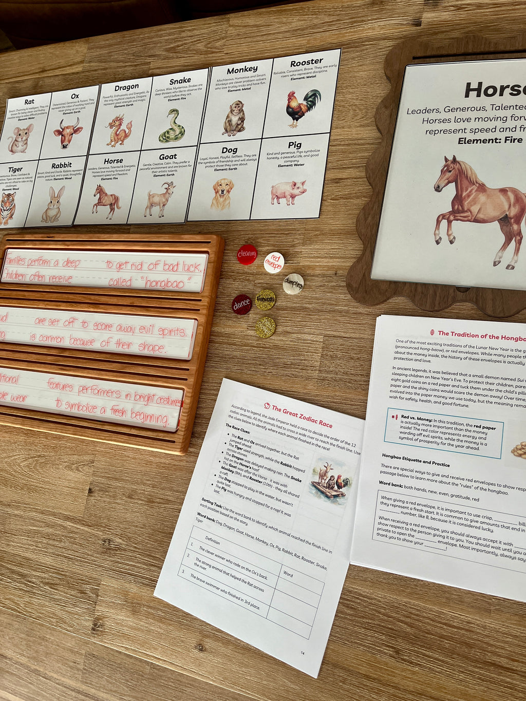 Digital Download | Lunar New Year Unit Study featuring printed learning sheets with zodiac animal illustrations, wooden trays holding dry erase marker practice, and small round sensory fillers, handcrafted homeschool education resources.