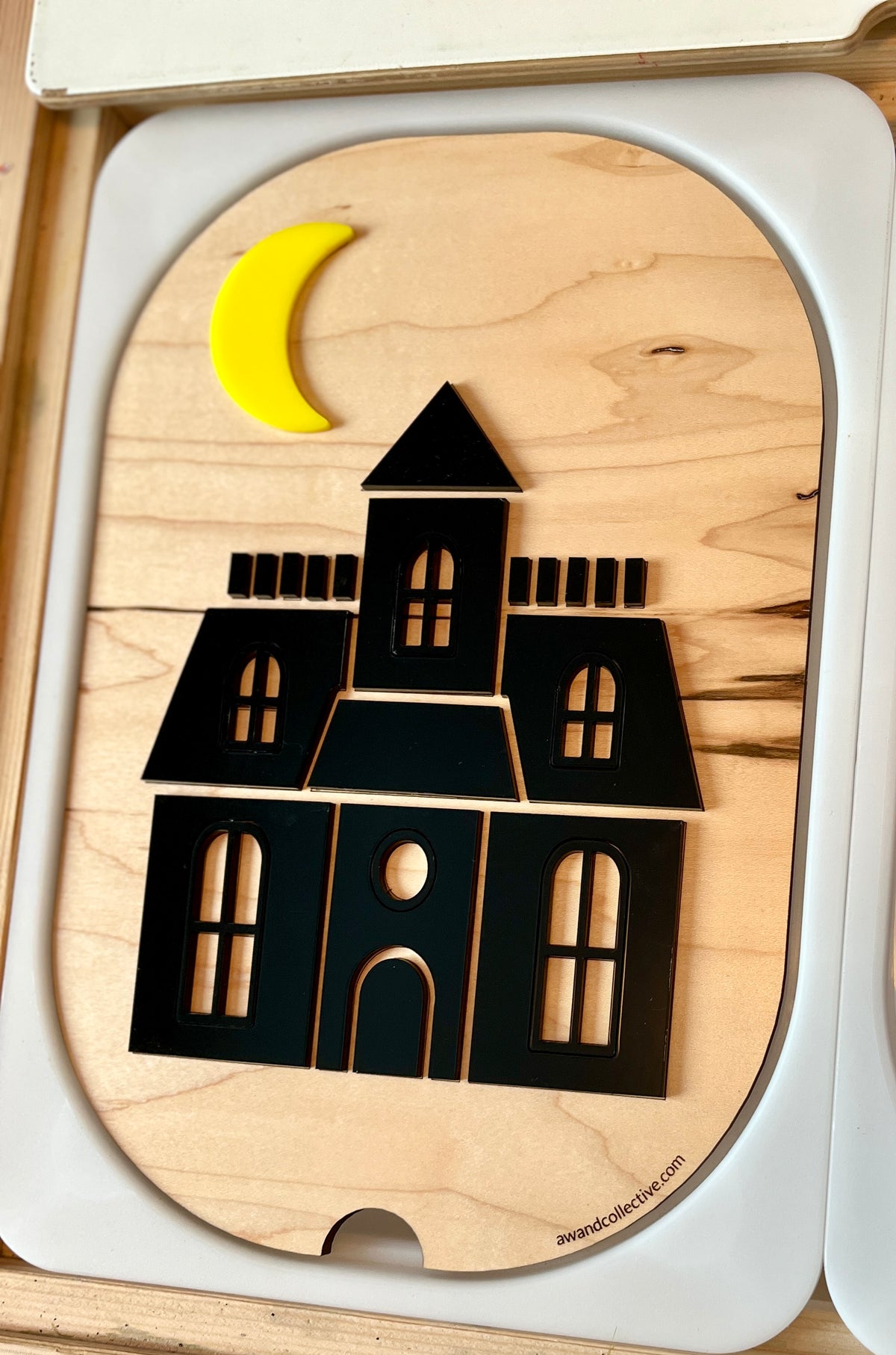 Black wooden haunted house puzzle with windows and doors under a yellow crescent moon on a natural wood base
