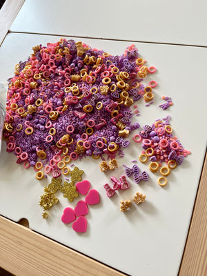 Princess-themed sensory kit with loose parts including glitter crowns, hearts, bows, and colorful rice on white surface