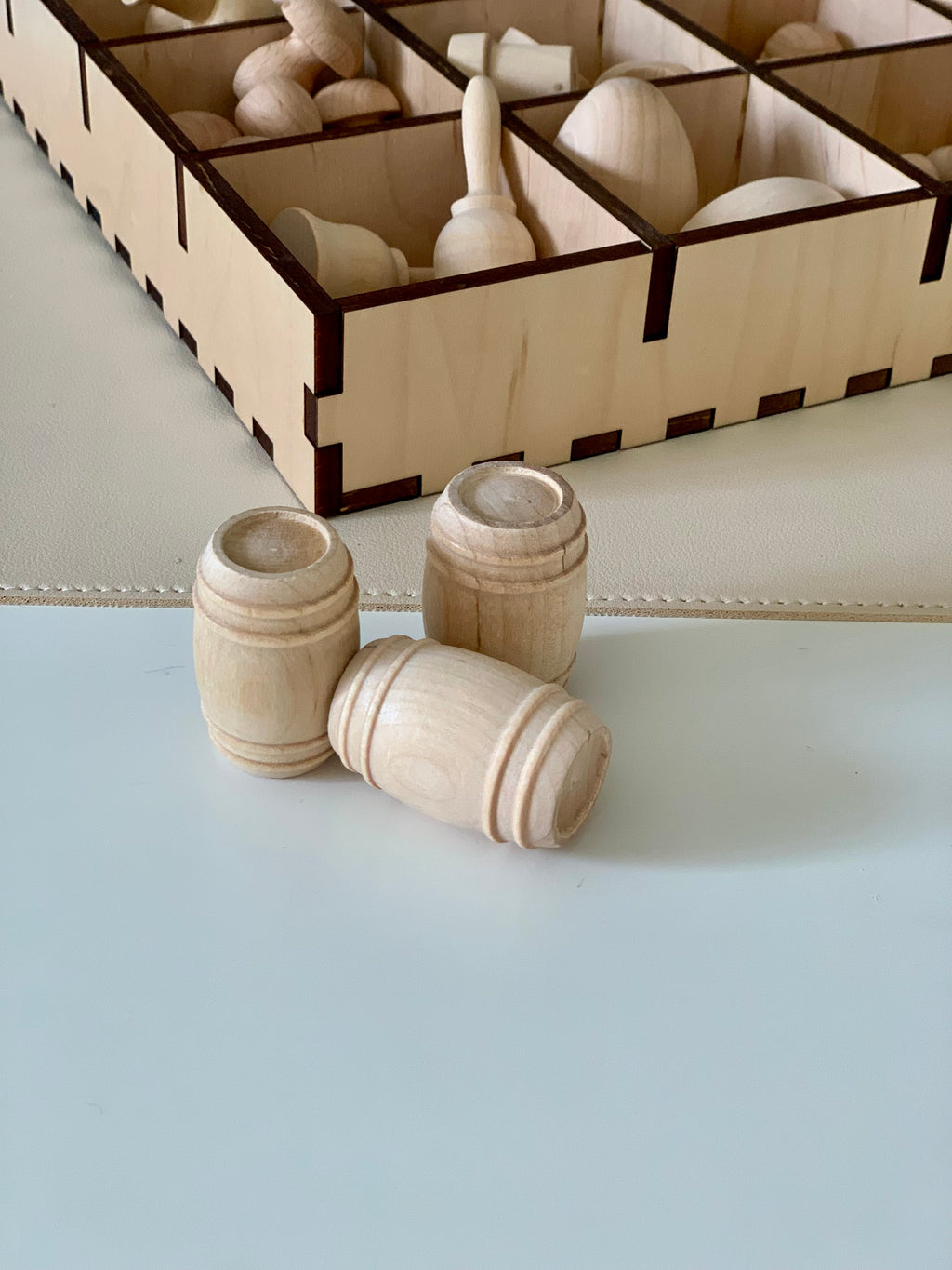 Three natural unfinished wooden barrel shapes placed on a smooth surface with a wooden compartment box in the background